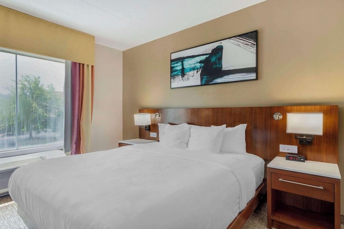 A hotel room with a large bed, bedside lamps, a nightstand, and a window with curtains.