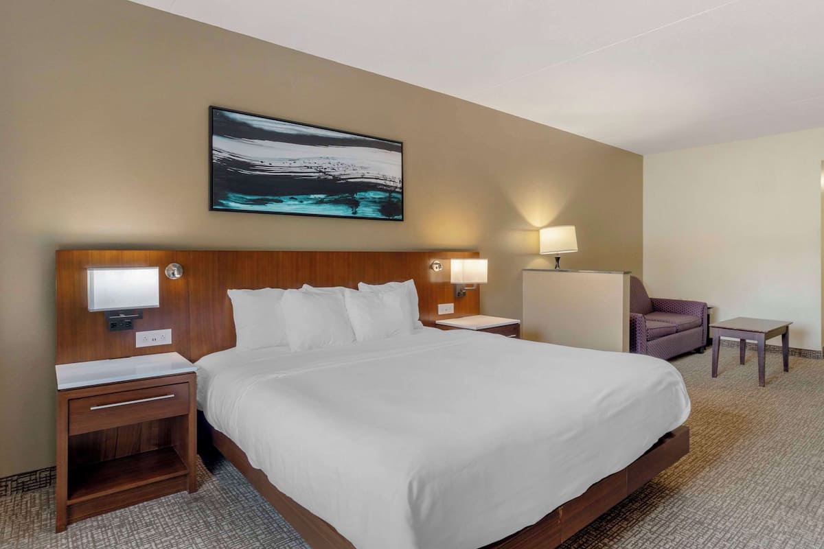 Une chambre d’hôtel avec un grand lit, deux tables de chevet, une chaise, une petite table et une lampe fixée au mur.