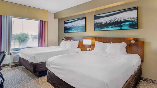 A hotel room with two beds, a large window with curtains, and two abstract paintings on the wall.