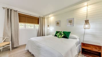 A bedroom with a bed, a bedside table, a chair, a window with curtains, and wall-mounted lights.