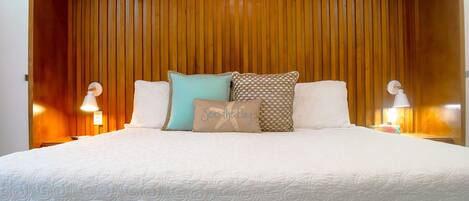 A neatly made bed with a white quilt, two bedside lamps, and three pillows with different patterns.
