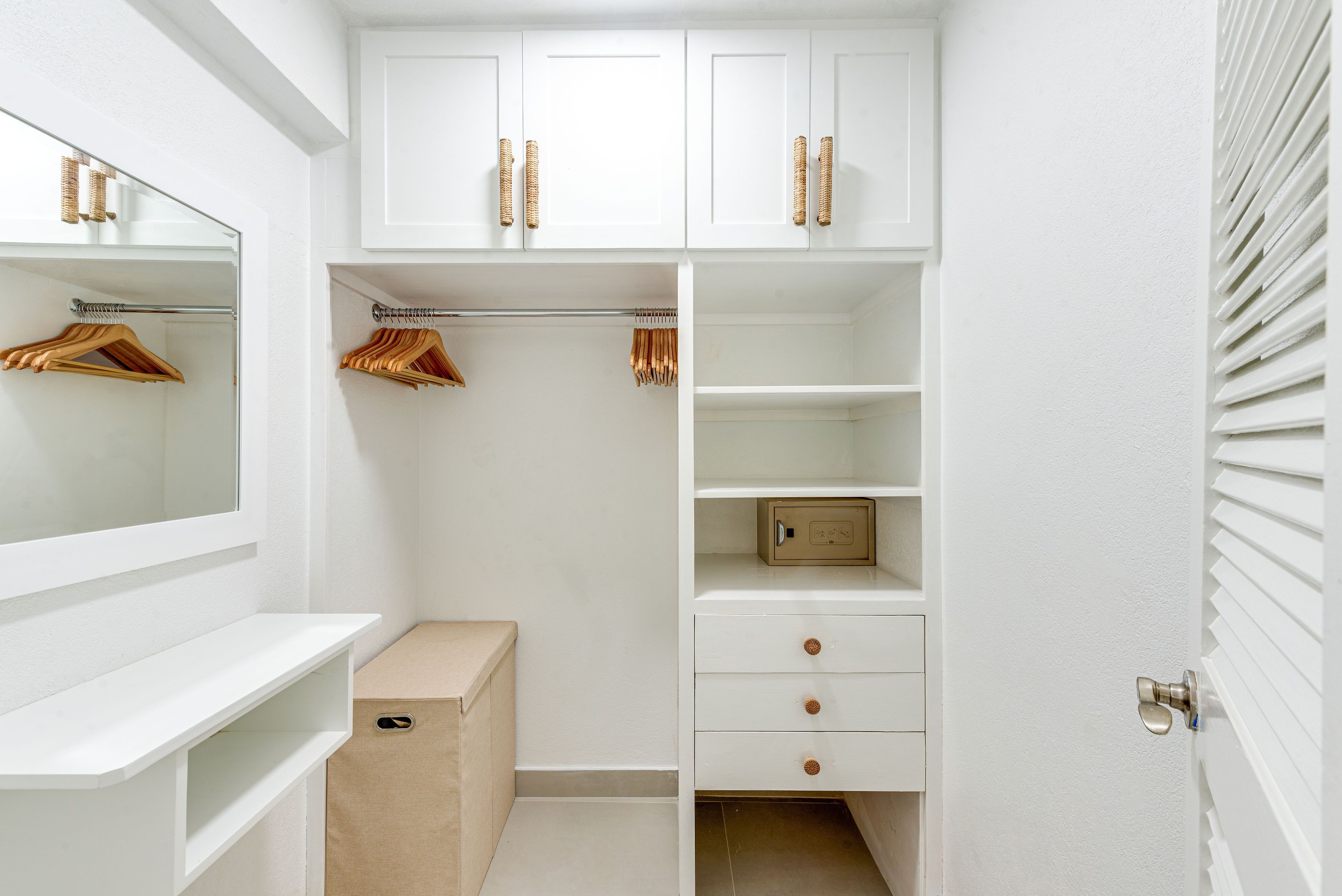 A white walk-in closet with wooden hangers, a mirror, and a small storage box.