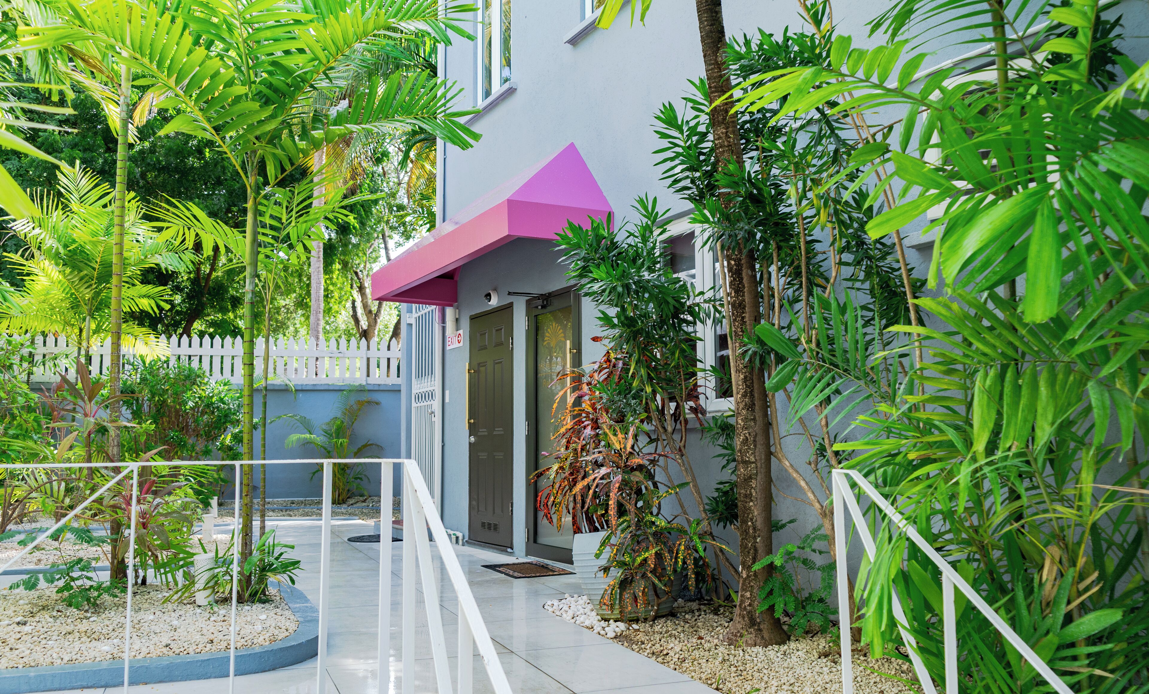 A modern building with a gated entrance, surrounded by lush greenery and a white fence.