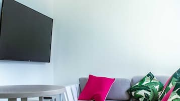 A modern living room with a grey sofa, a round white table, and a flat-screen TV mounted on the wall.