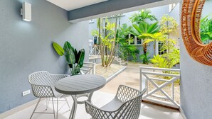 A modern patio with a round table and white chairs, surrounded by lush greenery and a view of a residential area.