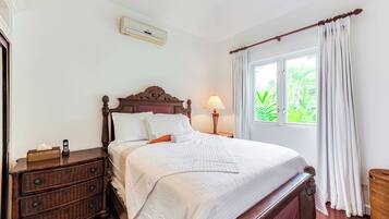 A neatly made bed with a wooden headboard, a bedside table with a lamp, and a window with curtains.