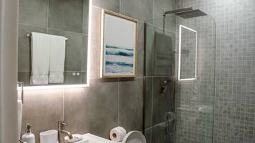 A modern bathroom with a glass shower enclosure, a large mirror, and a framed picture of the ocean.