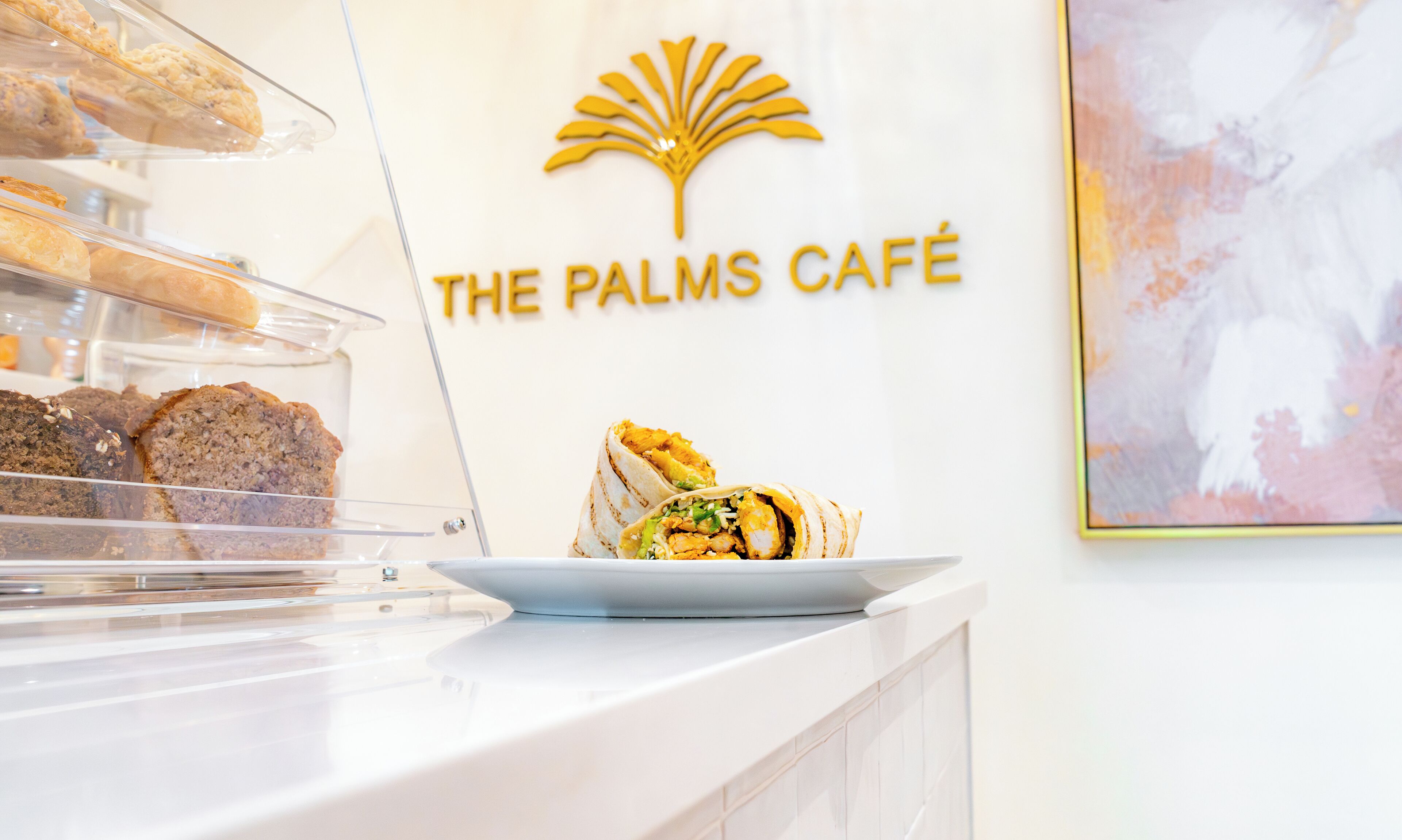 A café counter with pastries and a wrap. The café's logo is displayed above the counter.