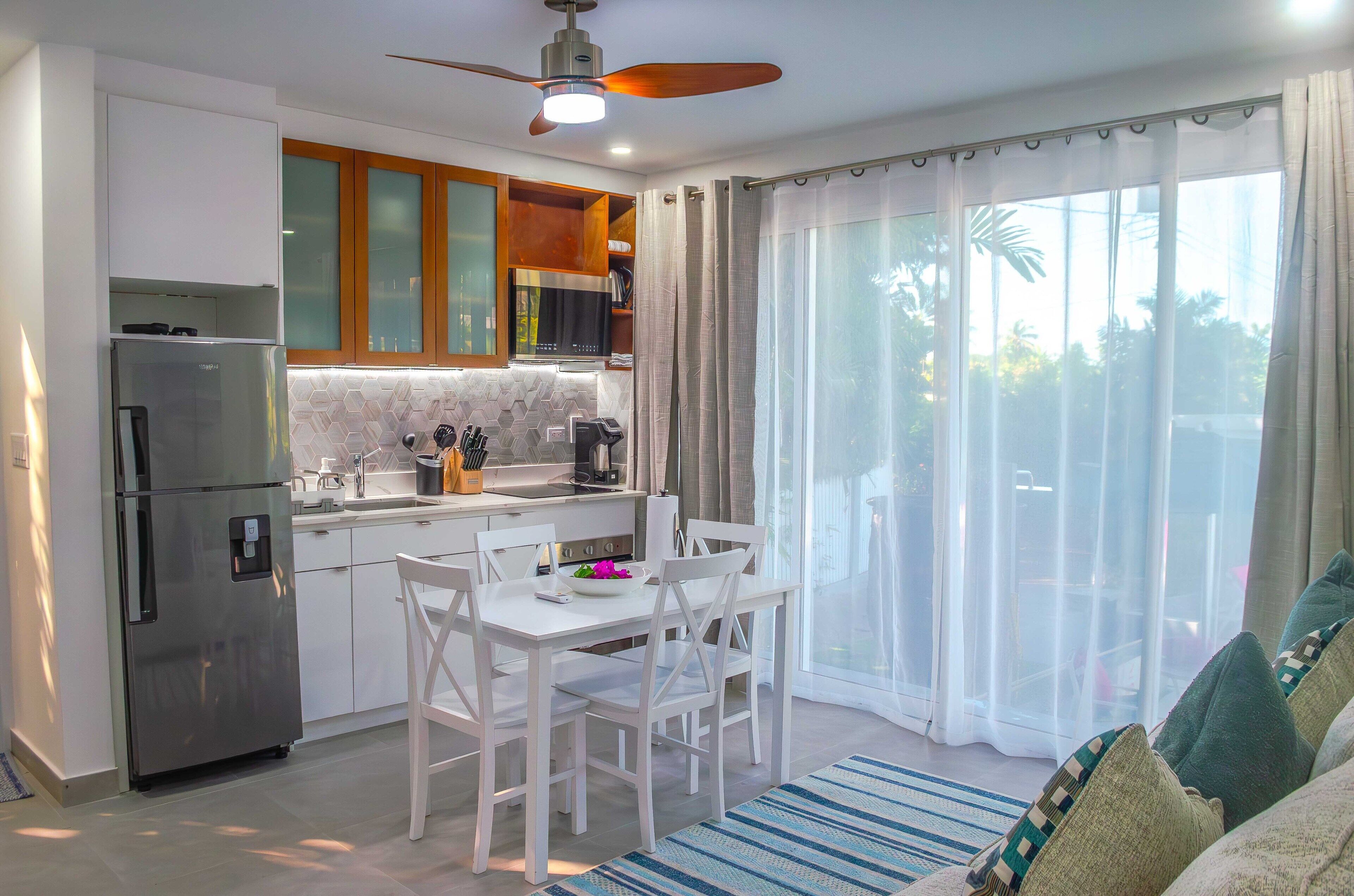 A modern kitchen with white cabinetry, a stainless steel refrigerator, and a dining area with a white table and chairs.