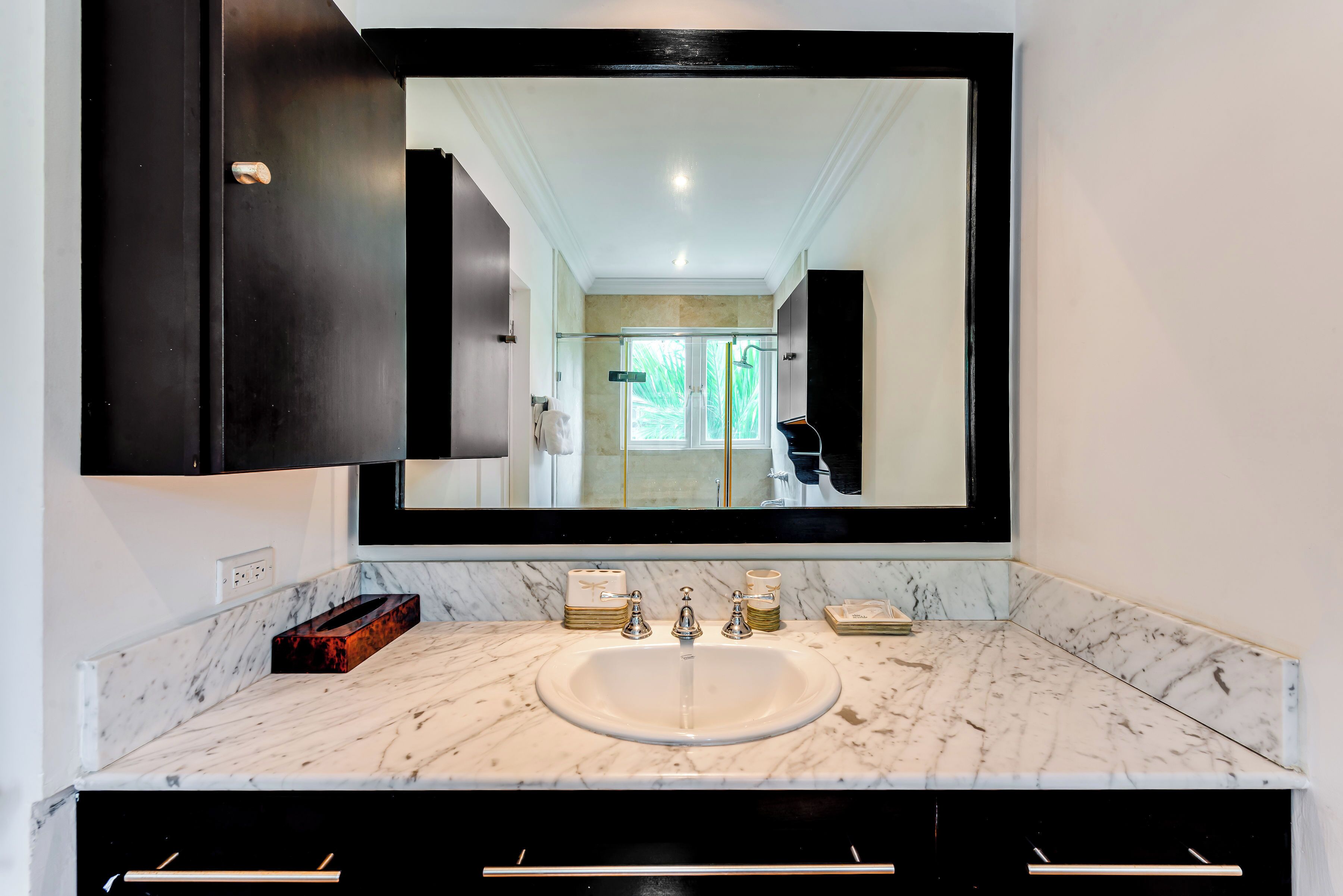 A bathroom with a large mirror, a marble sink, and dark cabinetry.