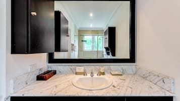 Une salle de bain dotée d’un grand miroir, d’un lavabo en marbre et de meubles de rangement aux couleurs sombres.