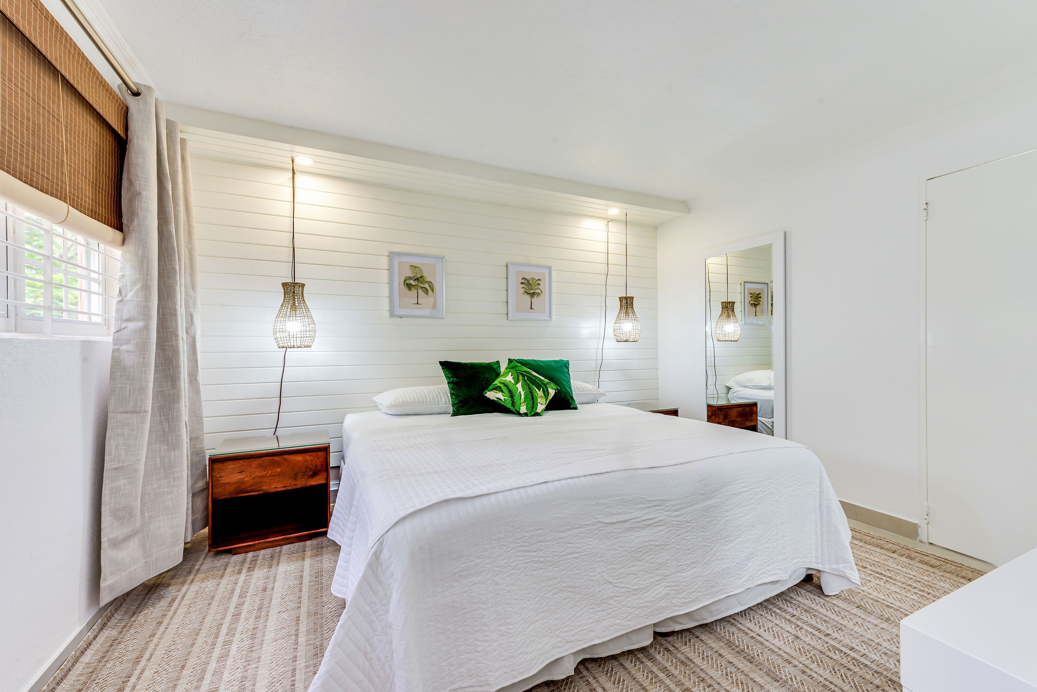 Un dormitorio con una cama grande, una mesita de noche de madera, un espejo y una ventana con cortinas.
