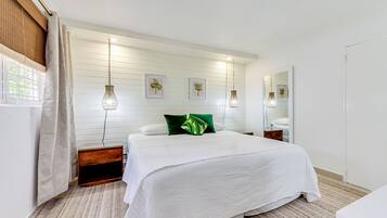 Un dormitorio con una cama grande, una mesita de noche de madera, un espejo y una ventana con cortinas.