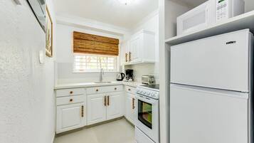 Une cuisine compacte avec des meubles blancs, un four encastré, un four à micro-ondes et un réfrigérateur.