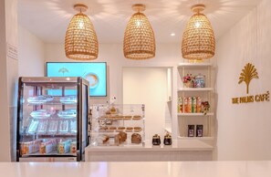 A café interior with a display case of pastries, a refrigerated display, and a shelf with beverages. - The Palms Resort (Holetown)