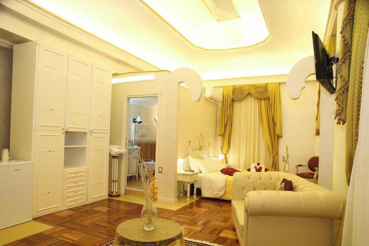 A hotel room with a bed, a sitting area with a sofa, a wardrobe, and a bathroom visible through an open door.