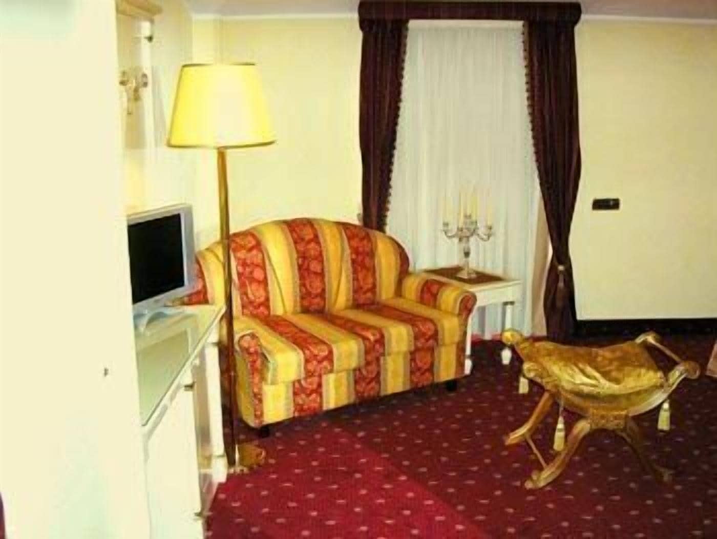 A room with a sofa, a lamp, a small table, a decorative chair, and a television.
