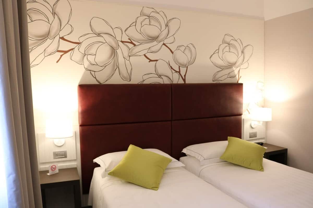 A hotel room with a large bed, two pillows, a red headboard, and wall art.