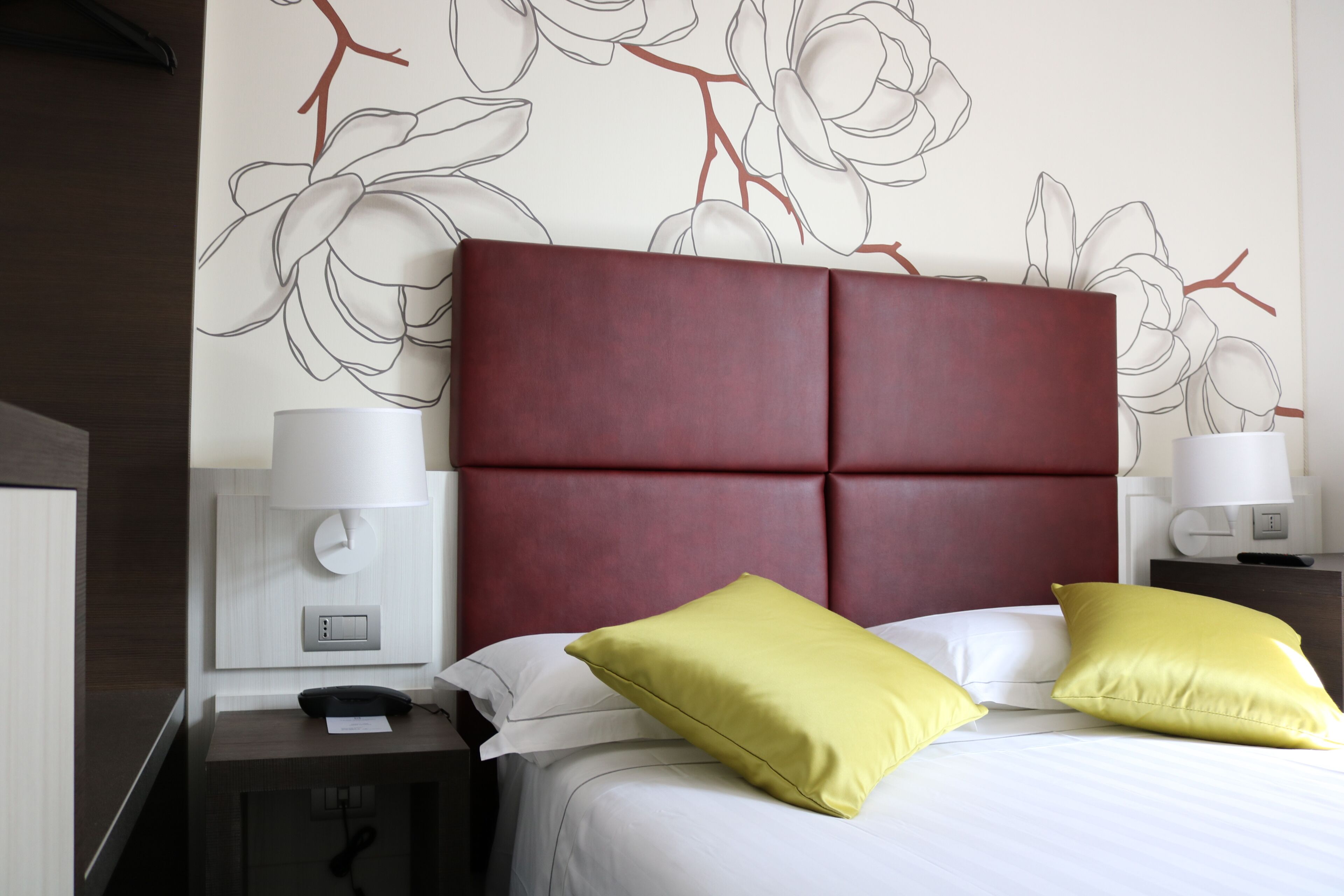 A hotel room with a large bed, two bedside lamps, a nightstand, and a wall with a floral design.