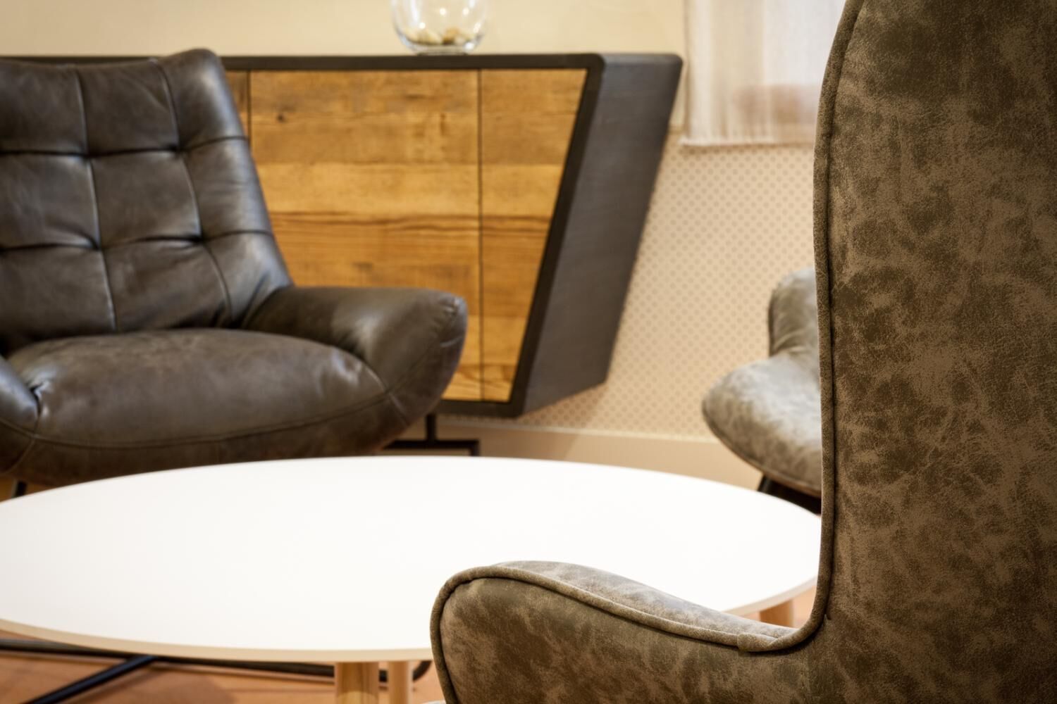 Een kamer met een bruine leren fauteuil, een witte ronde tafel en een houten kast.