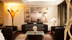 A modern living room with a glass coffee table, black leather sofas, and abstract wall art. - Hôtel Kyriad Strasbourg (Lingolsheim)