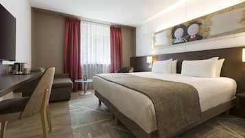 A hotel room with a large bed, a desk, a chair, a small table, and a painting on the wall.