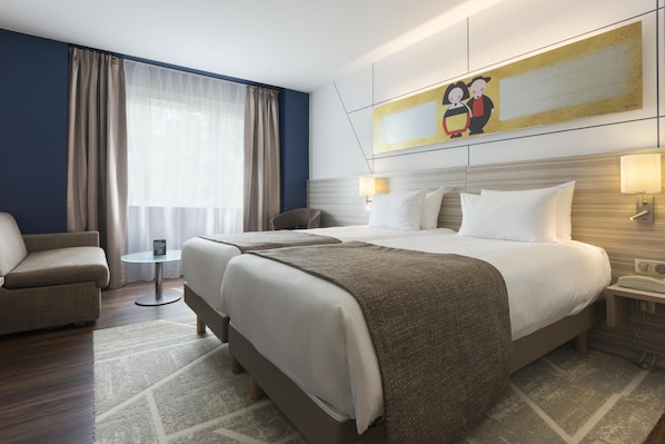 A hotel room with a bed, two bedside tables, a chair, a small table, and a painting on the wall. - Hôtel Kyriad Strasbourg (Lingolsheim)