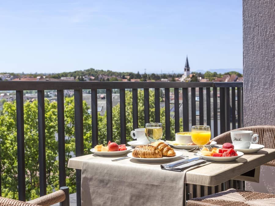 Un balcon avec une table préparée pour le petit-déjeuner, comprenant des croissants, des fruits et des boissons.