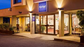 Welcome to the Kyriad Hotel, featuring a modern entrance with a glass door and outdoor seating area.