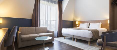 A hotel room with a bed, a sofa, a small table, and a chair.