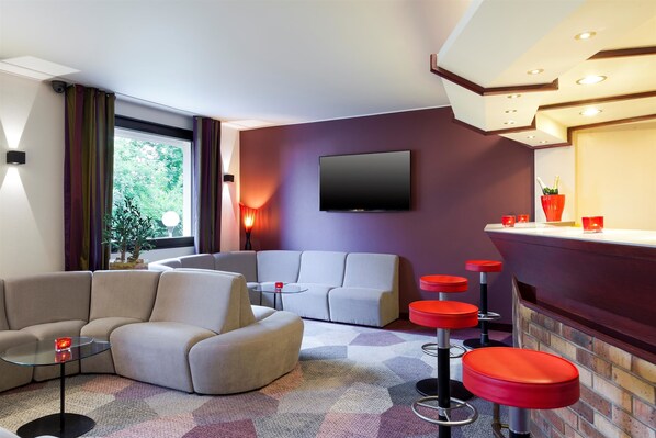 A modern living room with a sofa, a glass coffee table, and a bar area with red stools.