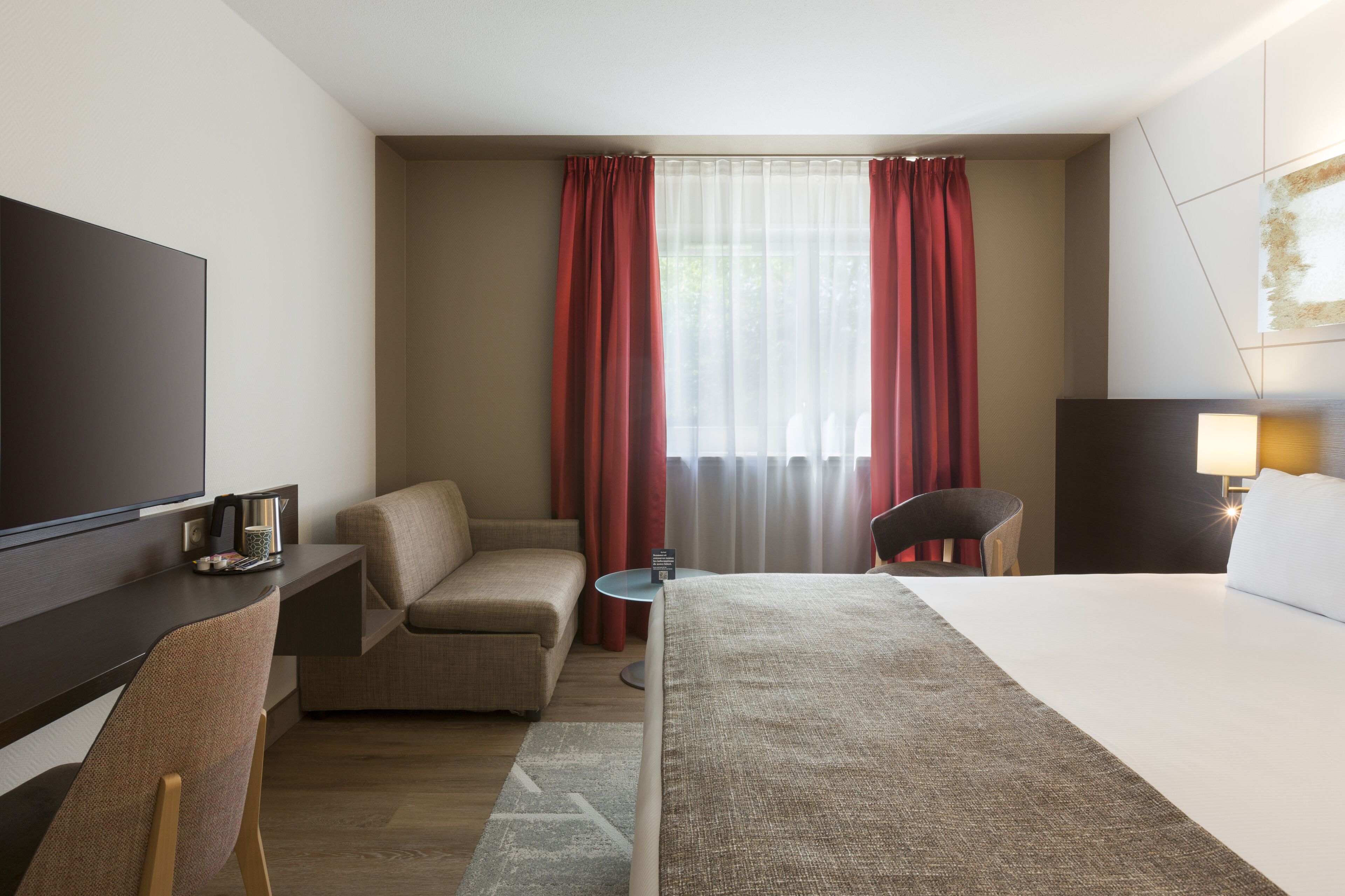 Una camera d'albergo con un letto, una scrivania, una sedia, una televisione e una finestra con tende.