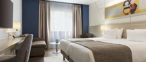 Habitación de hotel con cama, escritorio, silla, mesita y un cuadro en la pared.