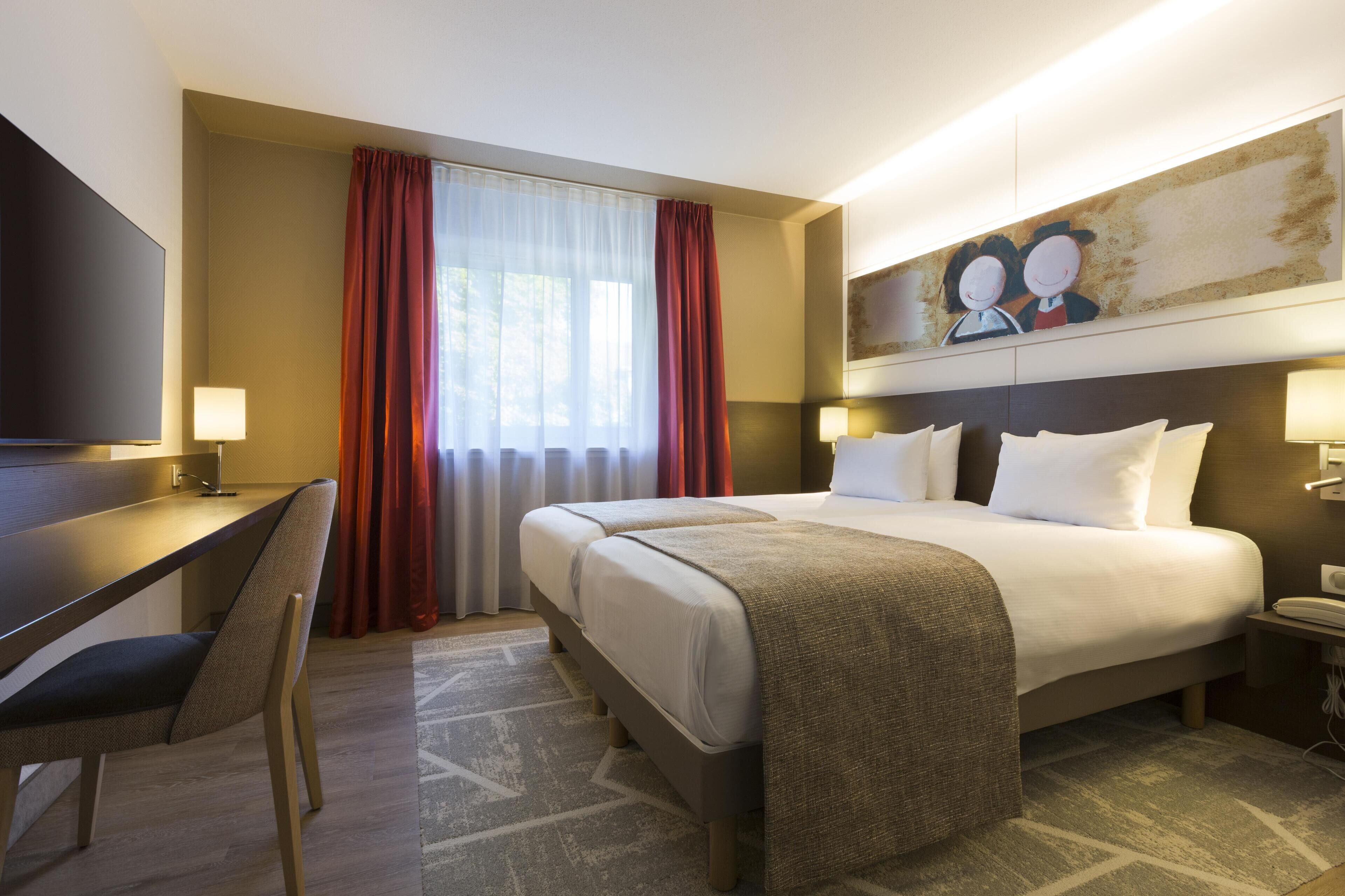 Une chambre d’hôtel avec un lit, un bureau, une chaise et un tableau au mur.