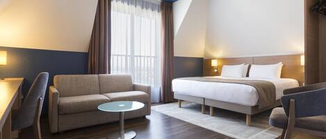 A hotel room with a bed, a sofa, a small table, and a chair.