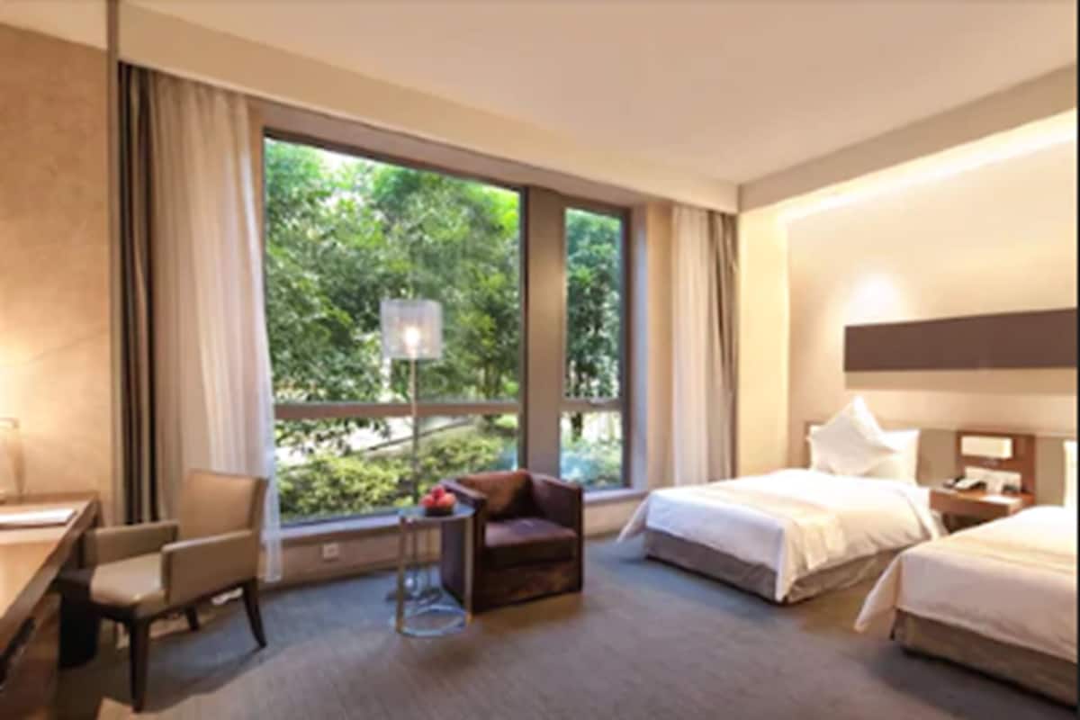 A hotel room with a large window, a bed, a desk, and a chair.