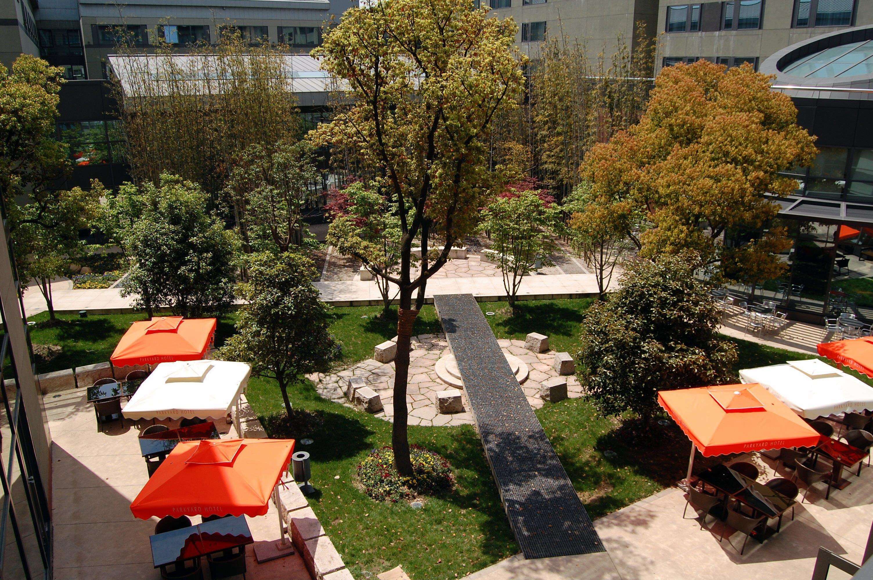 An outdoor patio area with multiple tables and chairs, surrounded by trees and a stone pathway.