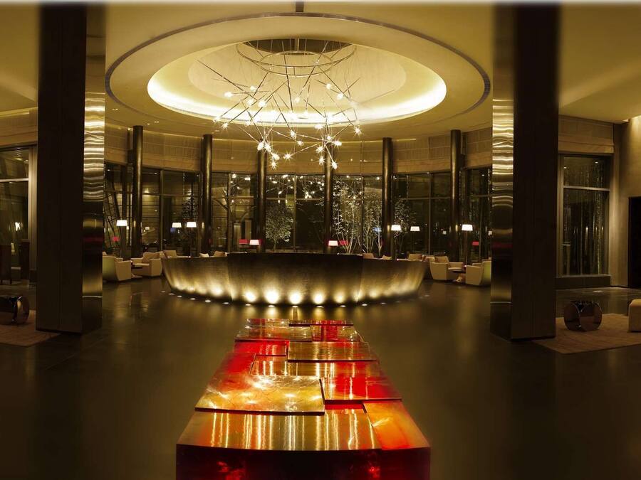 A modern lobby with a central seating area, a reception desk, and a large chandelier.