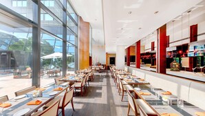 A spacious restaurant with long tables, chairs, and a large glass wall offering a view of the outdoors. - Shanghai Zhangjiang Parkyard Hotel (Shanghai)