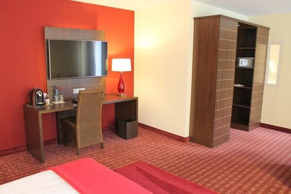 A hotel room with a bed, a desk with a chair, a TV, a lamp, and a wardrobe.