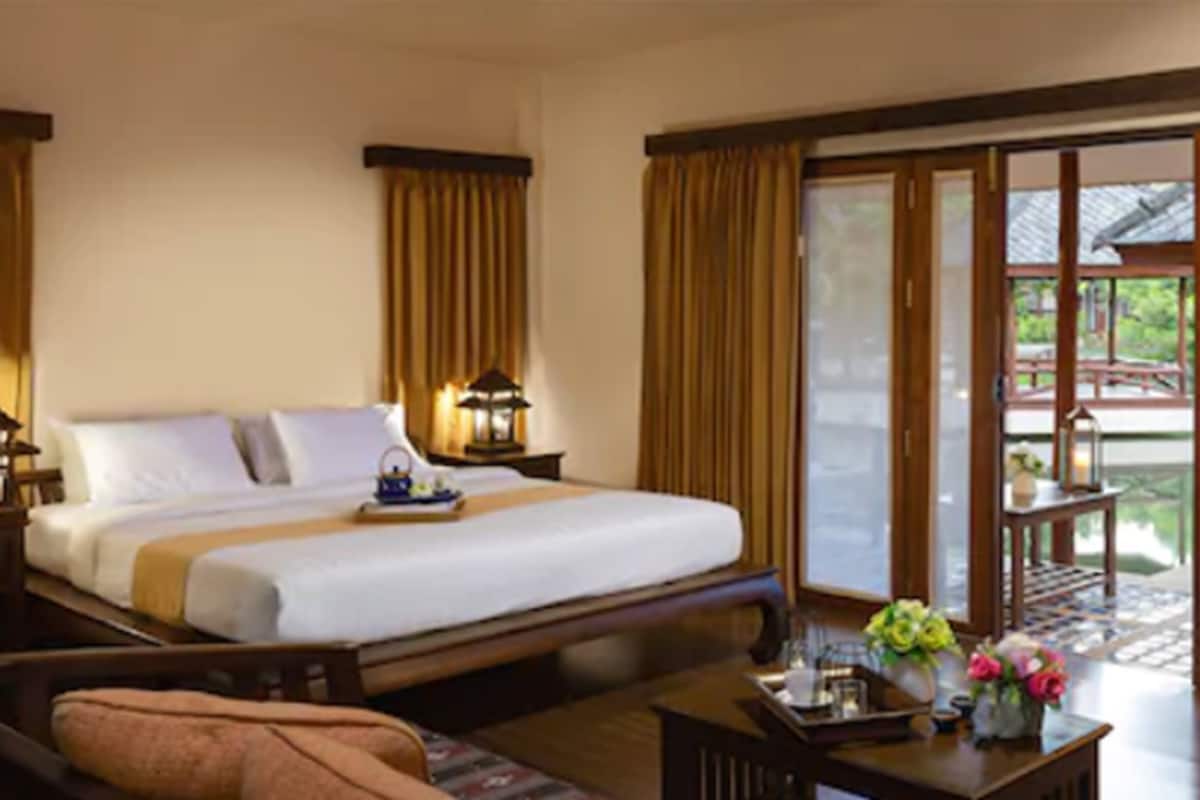 A hotel room with a large bed, a sofa, a small table with flowers, and a balcony with a view.