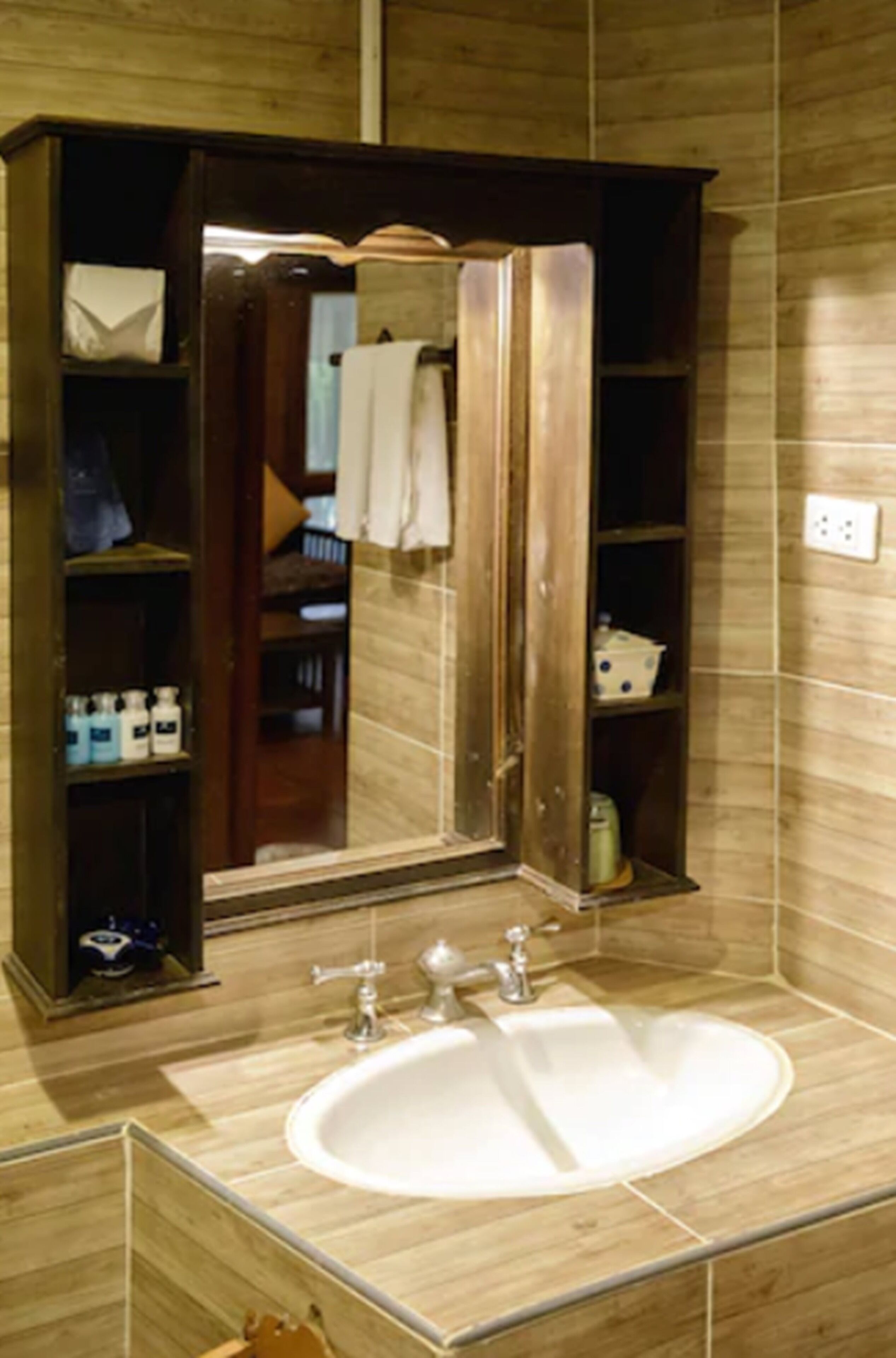Un baño con un espejo grande, un lavabo blanco y un mueble de tocador de madera con estantes.