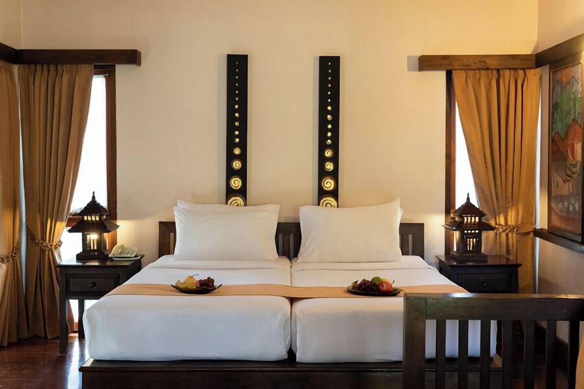 A double bed with two nightstands, each with a lantern, and a painting on the wall.