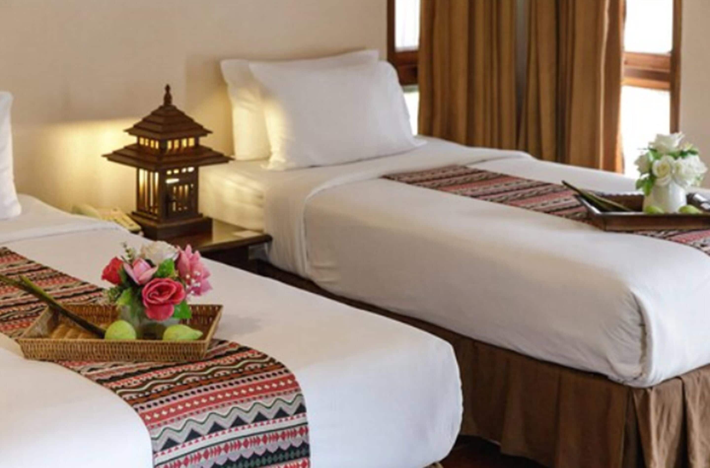 Ein Hotelzimmer mit zwei Betten, einem Nachttisch mit einer Laterne und einem dekorativen Tablett mit Blumen.