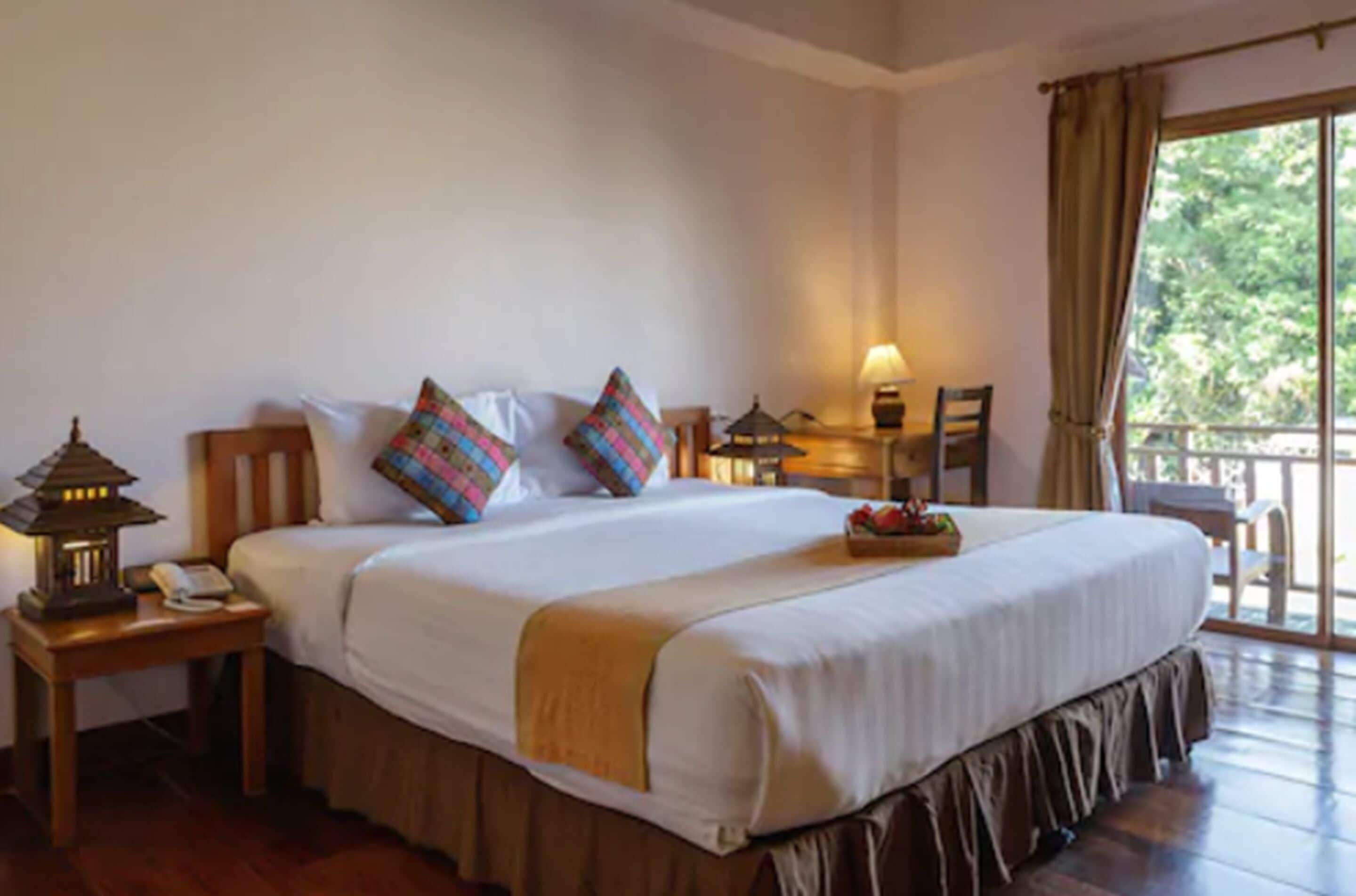 A hotel room with a large bed, a nightstand with a lamp, a chair, and a view of the outdoors.