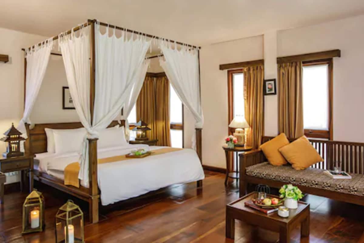 A bedroom with a four-poster bed, a sofa, a nightstand, and a bedside table with a lamp.