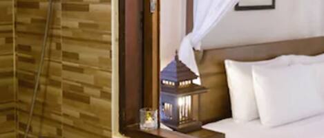 A hotel room with a wooden floor, a bed with white bedding, a shower area, and a small table with a vase of flowers.