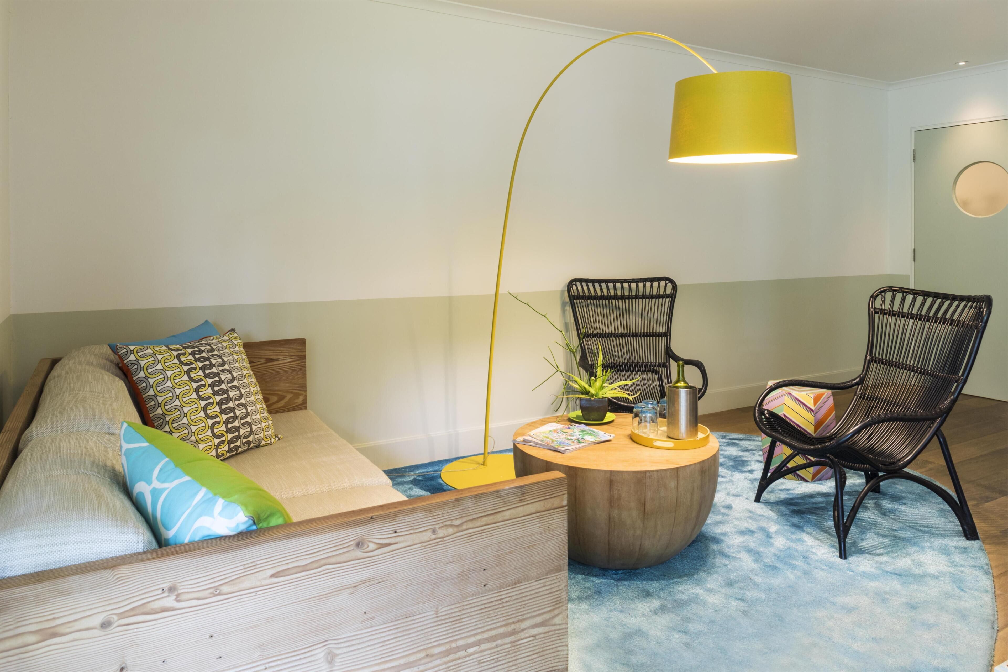 A modern living room with a wooden sofa, two black wicker chairs, a round coffee table, and a yellow lamp.