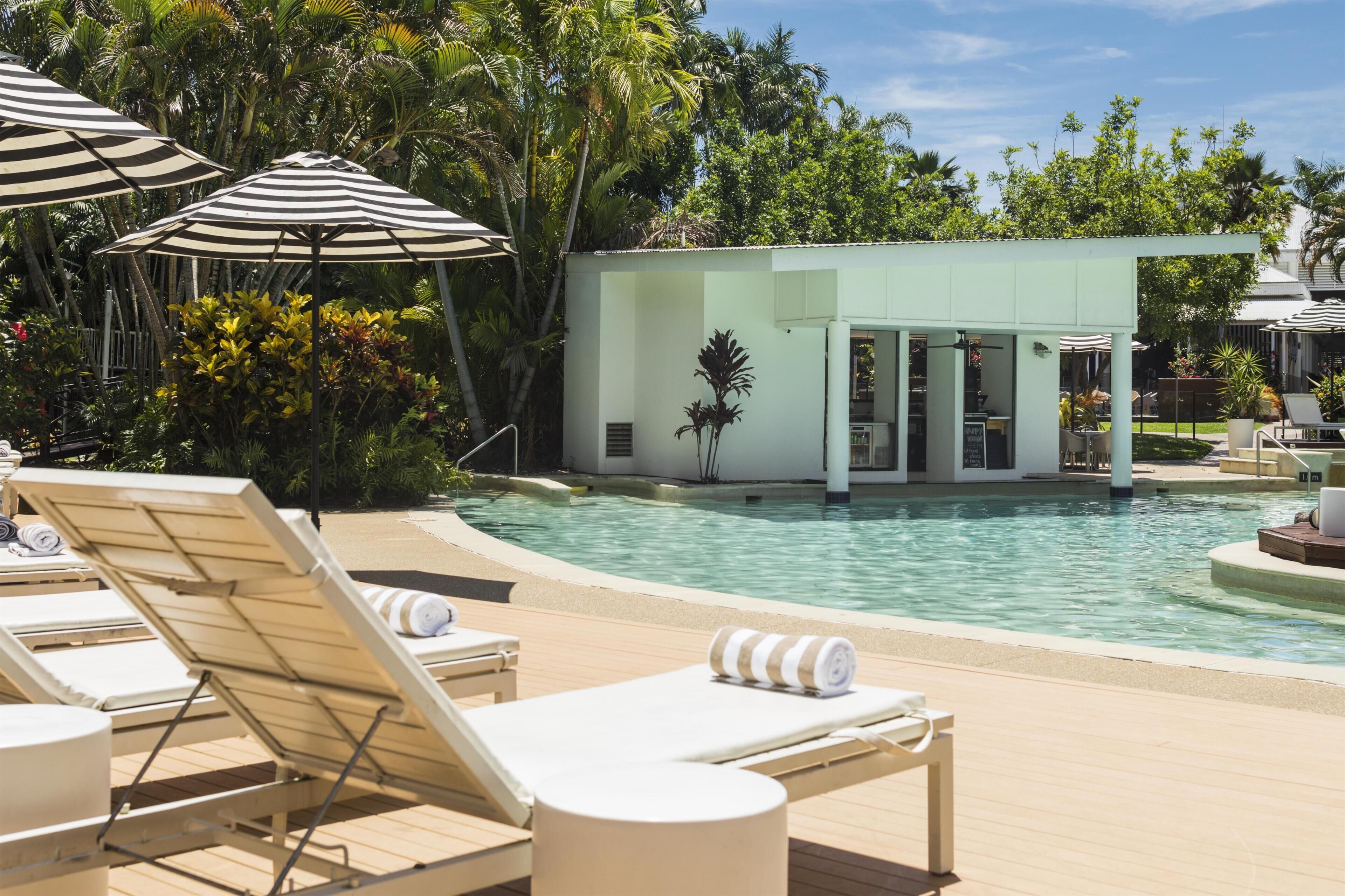 A pool area with lounge chairs and umbrellas, surrounded by lush greenery.