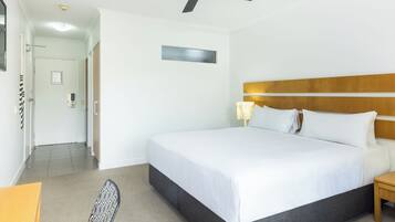 A hotel room with a bed, a ceiling fan, a nightstand, a lamp, and a chair.